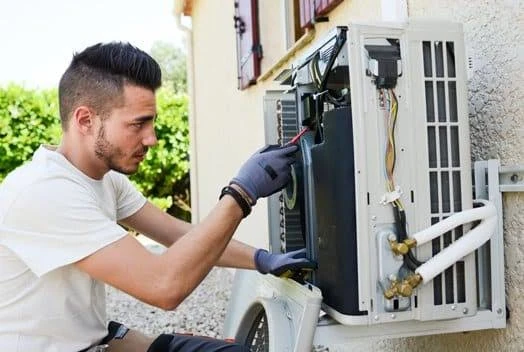 Technician servicing a wall-mounted outdoor heat pump unit